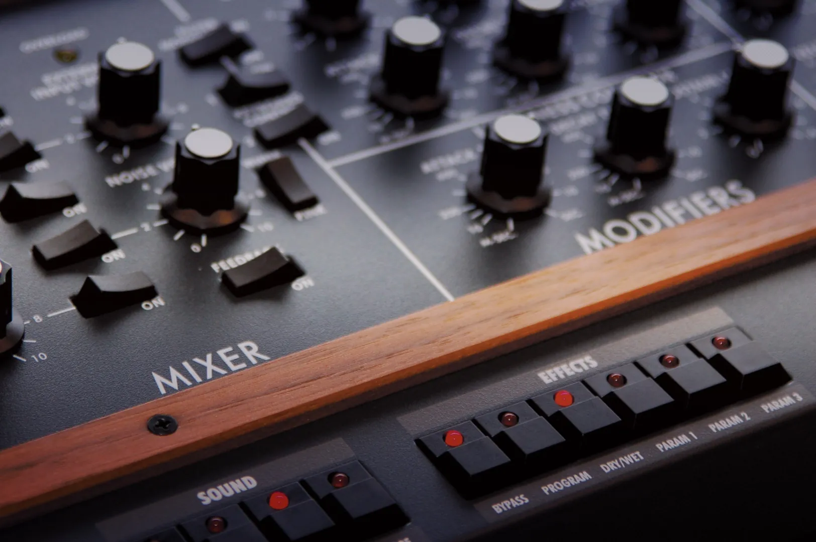 Close-up of an analog synthesizer control panel showing mixer and modifiers sections with black knobs, faders, and wooden trim, ideal for electronic music production and sound design.